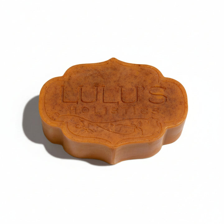 A single scalloped Lulu's Holistics Pineapple & Turmeric Mango Butter Bar Soap in a warm, speckled orange-yellow color, featuring the embossed brand logo on the front.