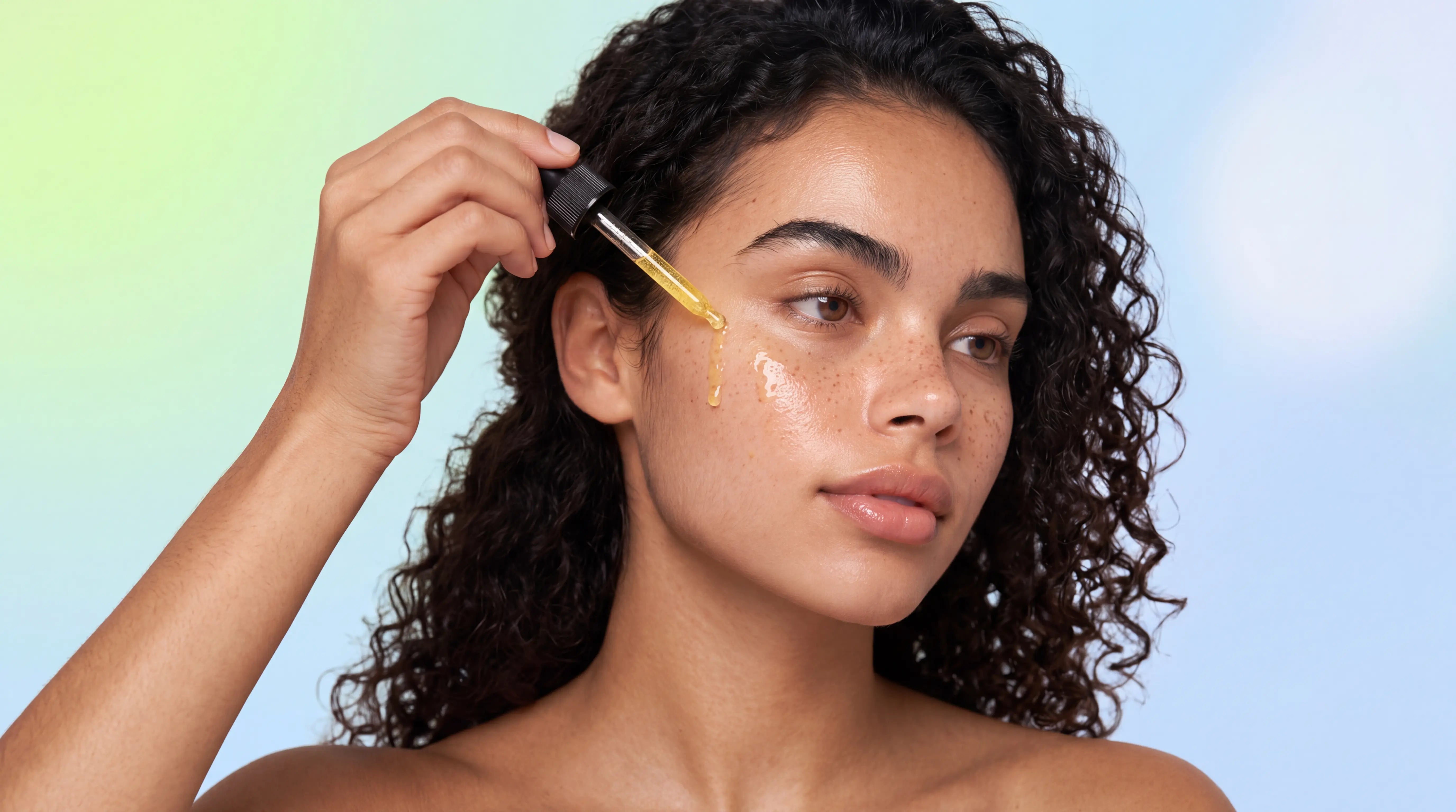 Model applying golden Lulu's Holistics Hyaluronic Acid Hydrating and Lightening Serum to face with a glass dropper