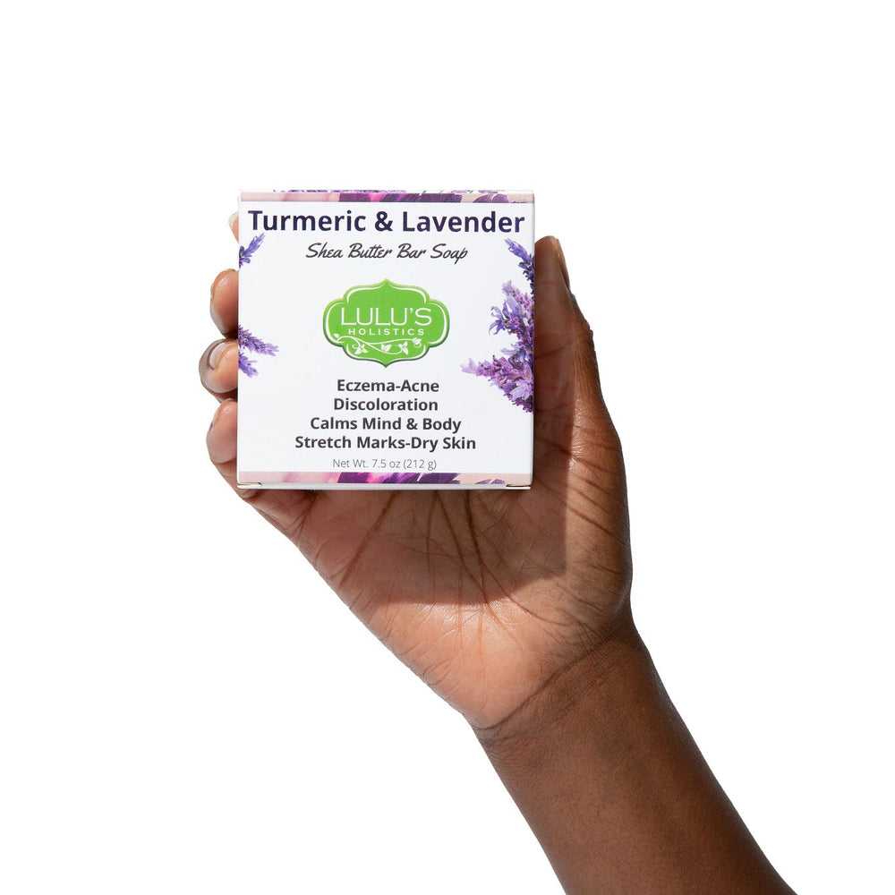 Hand holding a box of Lulu's Holistics Turmeric and Lavender Shea Butter Bar Soap. A US-crafted natural daily cleanser formulated to target eczema, acne, and discoloration while calming sensitive skin.