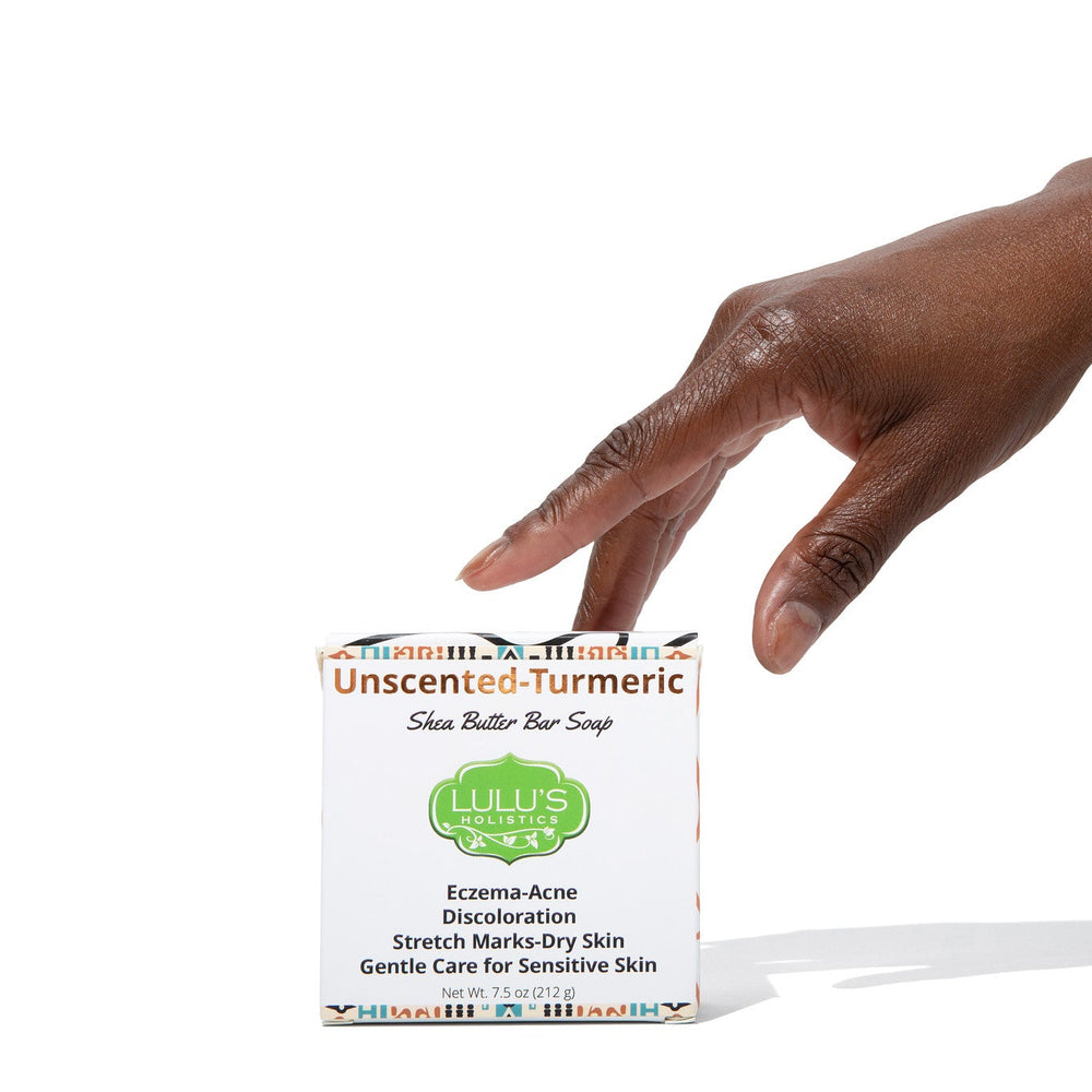 Hand reaching for the Lulu's Holistics Unscented Turmeric Shea Butter Bar Soap box. A powerful, 100% fragrance-free daily cleansing treatment explicitly formulated to target eczema, body acne, stretch marks, and stubborn discoloration, delivering deep moisture and natural hyperpigmentation relief for highly reactive and sensitive skin.