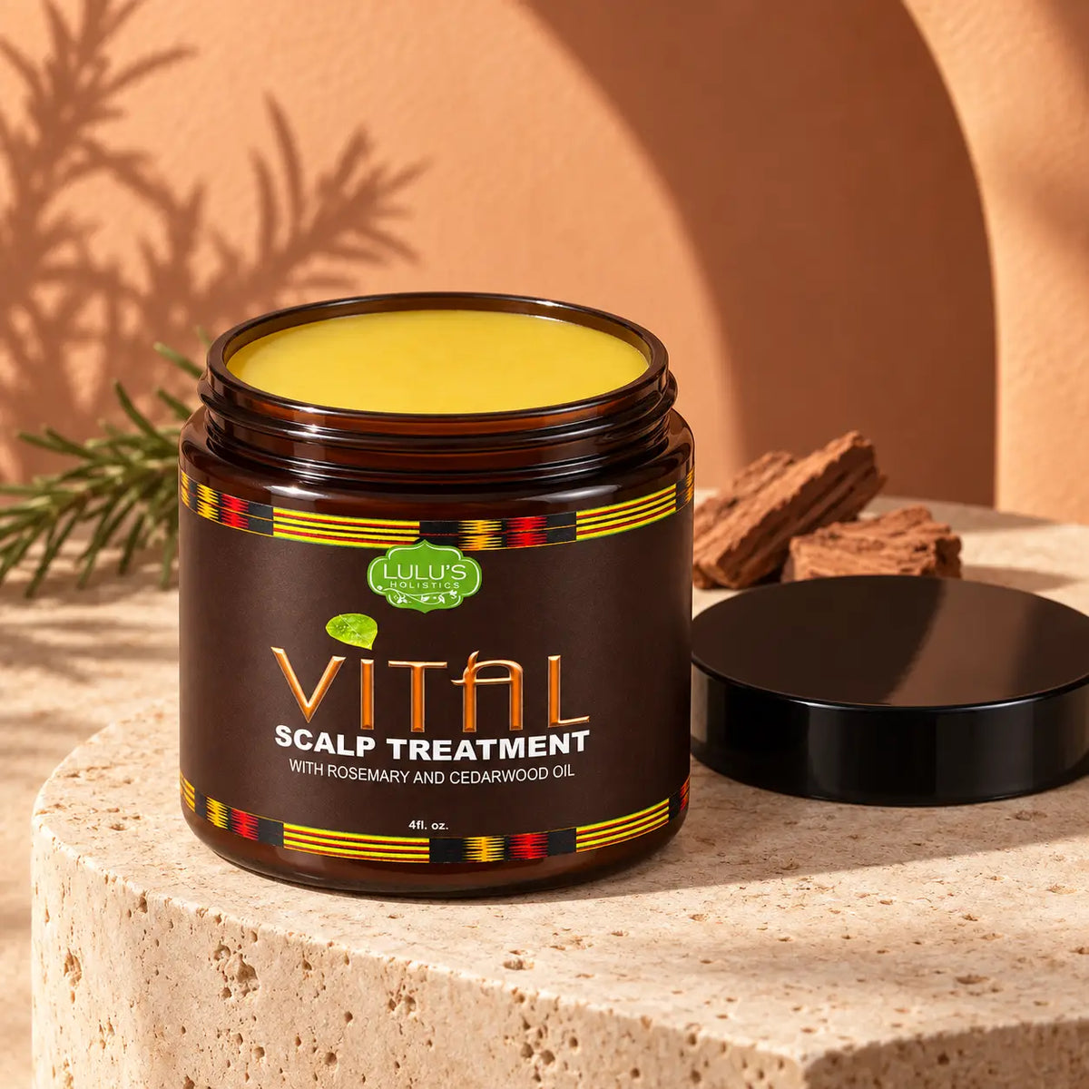 Open jar of Lulu's Holistics Vital Scalp Treatment displaying rich yellow ointment on a stone pedestal with fresh rosemary sprigs and cedarwood bark pieces