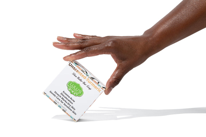 Hand holding a bar of Lulu's Holistics Unscented Turmeric Shea Butter Bar Soap on a crisp white background